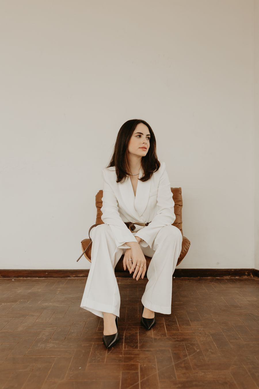 Marcela Lamastra de terno branco, sentada em uma poltrona